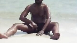 Watch this horny dude stroke his big black dick and jerk off on the beach